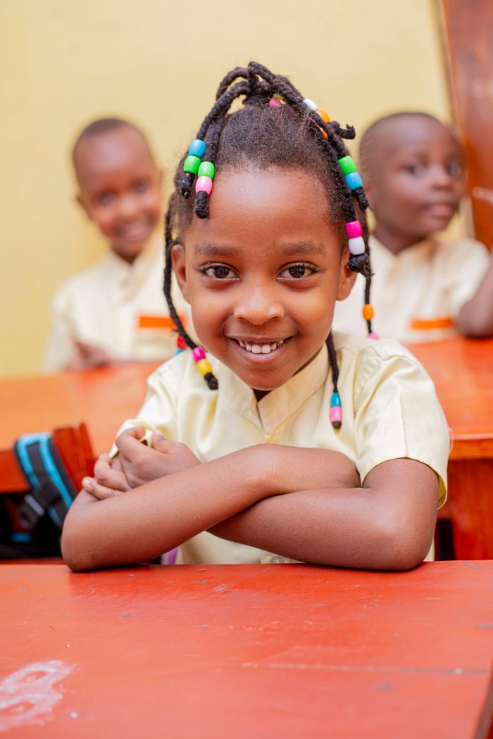 Mastering the First Impression: Your intriguing post title goes here Adorable African girl with braids smiling in classroom, arms crossed on desk.