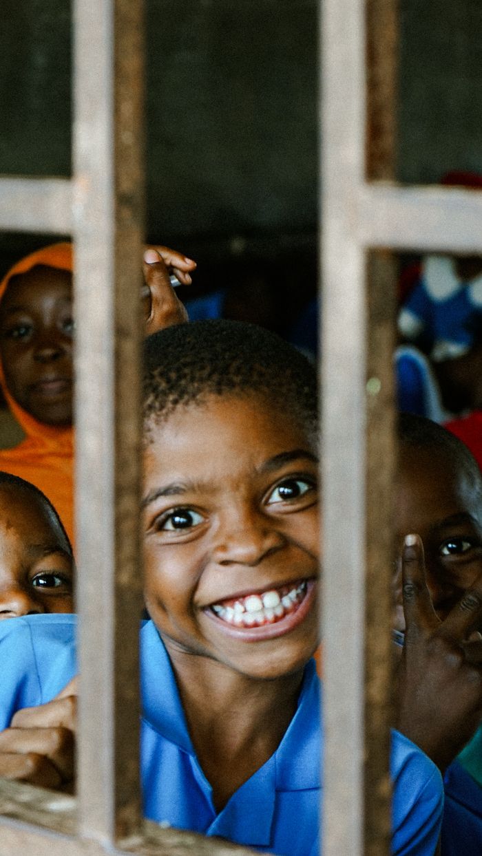 Smiling African children peek through window bars, capturing genuine joy.